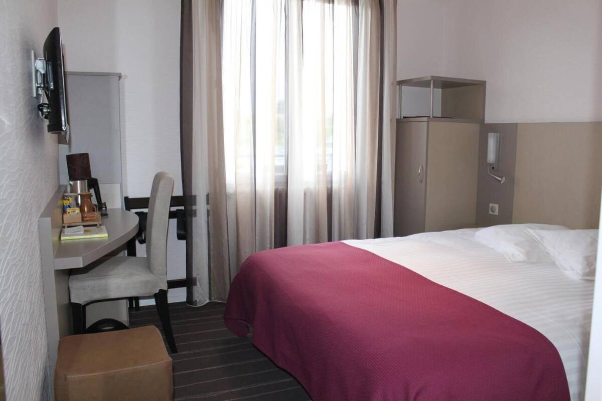 A hotel room with a bed, a desk with a chair, a television, and a wardrobe.