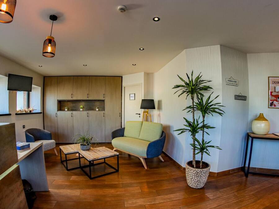 Una sala de estar moderna con un sofá, una mesa de centro y una planta en maceta. Se observa un mueble de madera y un televisor fijado a la pared.