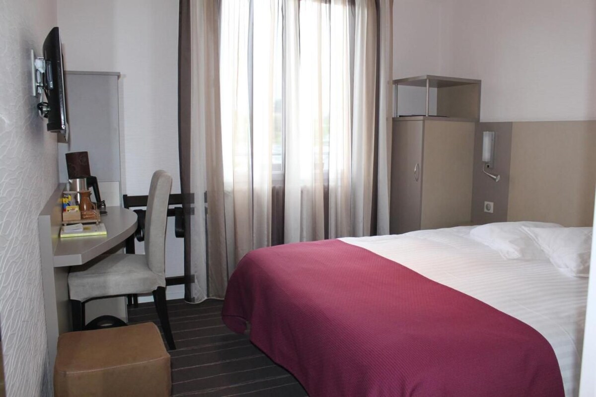 Habitació d'hotel amb llit, escriptori amb cadira, televisió i armari.