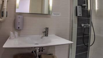 Un baño moderno con un lavamanos blanco, una cabina de ducha con paredes de vidrio y un espejo sobre el lavamanos.