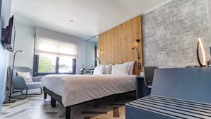 A modern hotel room with a large bed, a desk, a chair, and a view of greenery outside. - Hotel Du Parc (Perros-Guirec)