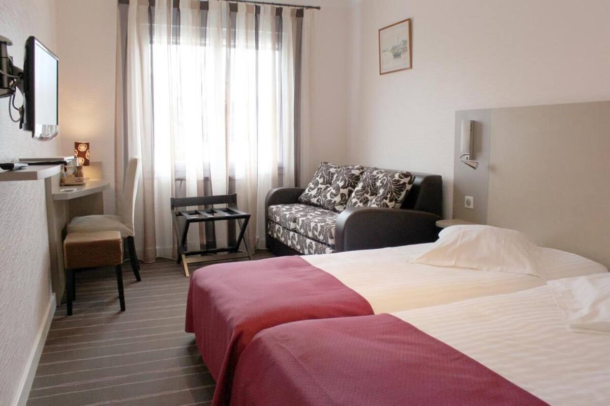 A hotel room with a bed, a sofa, a desk with a chair, a television, and a window with curtains.