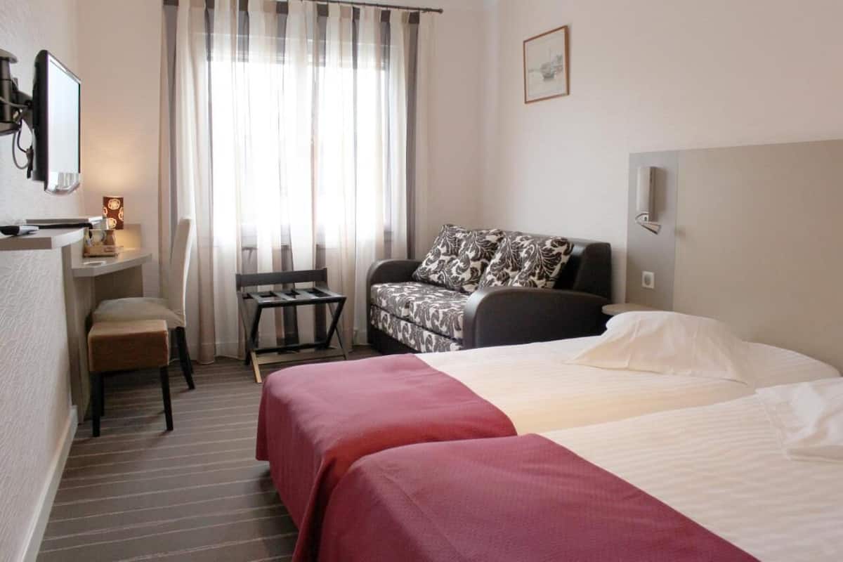 A hotel room with a bed, a sofa, a desk with a chair, a television, and a window with curtains.