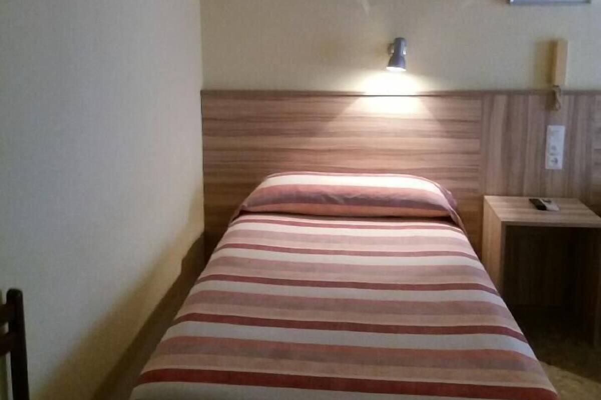 Un lit simple avec une literie à rayures, dans une chambre dotée d’une tête de lit en bois et d’une table de chevet.