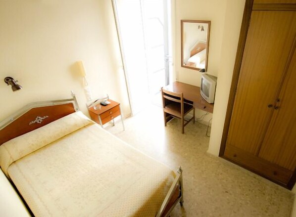 A bedroom with a bed, a desk with a chair, a television, a wardrobe, and a mirror on the wall. - Hotel Borja (Puig)