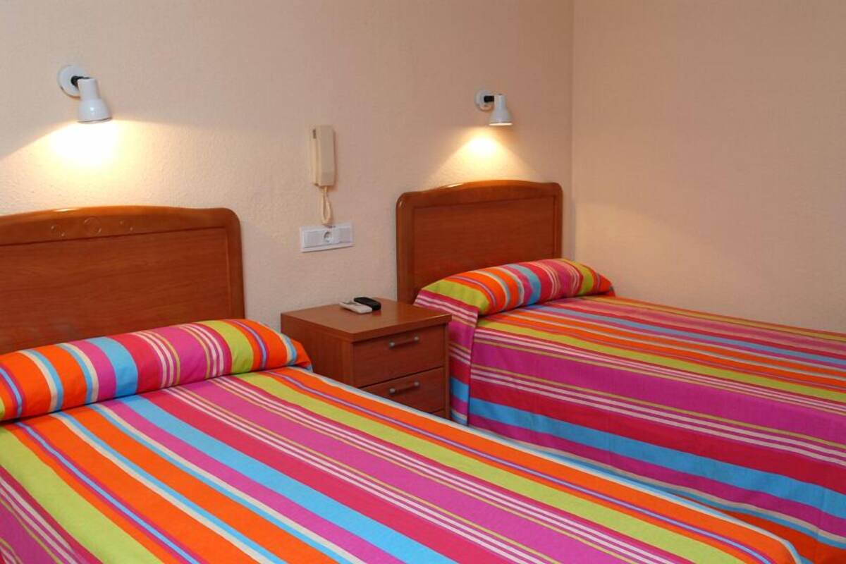 Une chambre avec deux lits, chacun recouvert d’une couvre-lit à rayures, doté d’une tête de lit en bois, d’une table de chevet et d’un téléphone fixé au mur.