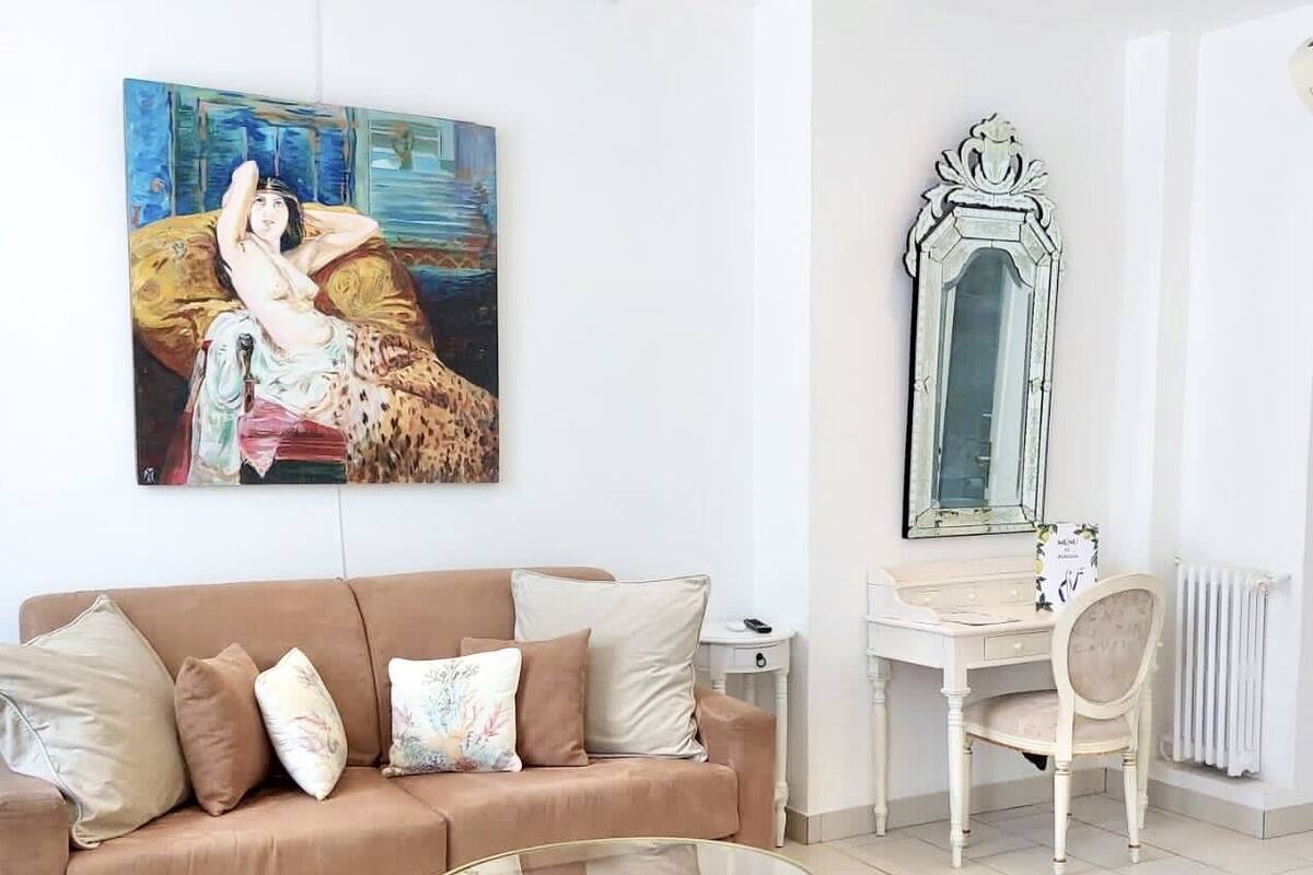 A modern living room with a beige sofa, a glass coffee table, a painting on the wall, and a decorative mirror.