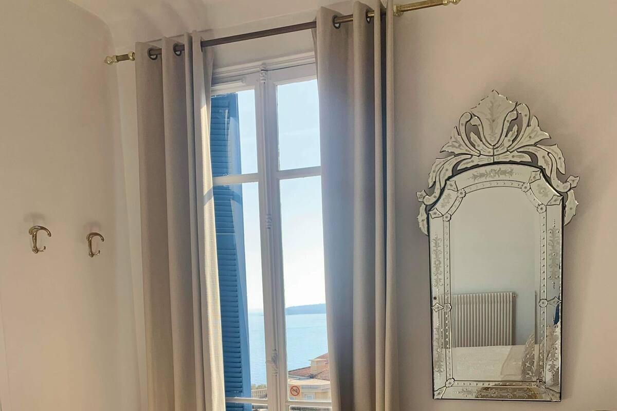 A hotel room with a bed, a chair, a mirror, and a view of the sea.