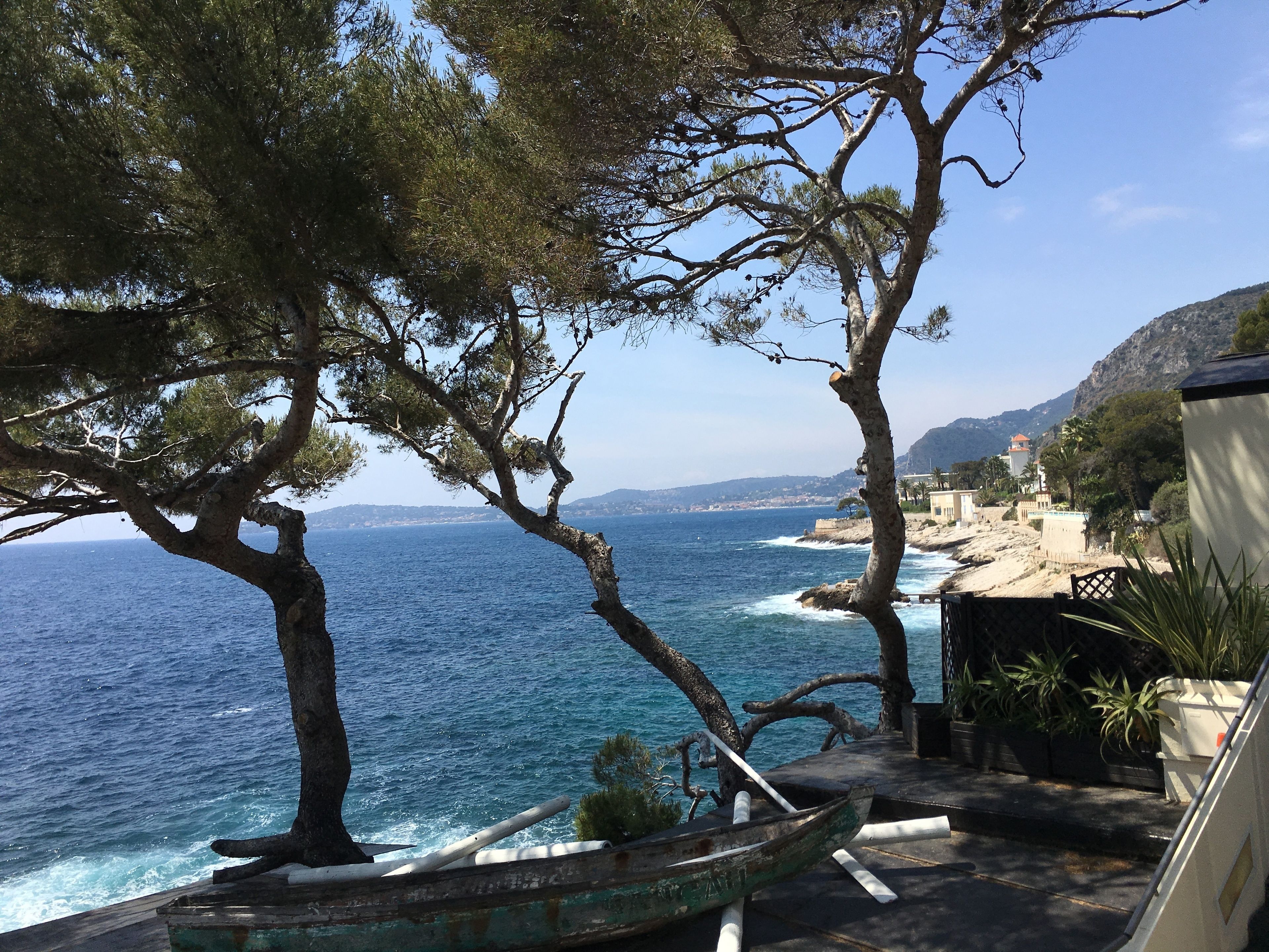 Une vue sur la côte, avec un rivage rocheux, un bateau et un bâtiment doté d’un toit rouge.