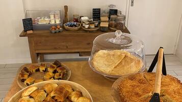 A buffet table with various baked goods, including croissants and pies, and a menu board in the background.