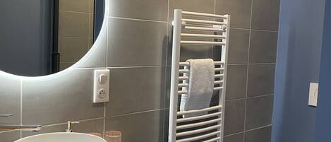 Un baño con un espejo redondo, un lavabo blanco, un perchero para toallas y un inodoro.