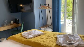Habitación de hotel con cama, televisor montado en la pared, escritorio con silla, perchero y vistas al exterior a través de una puerta.
