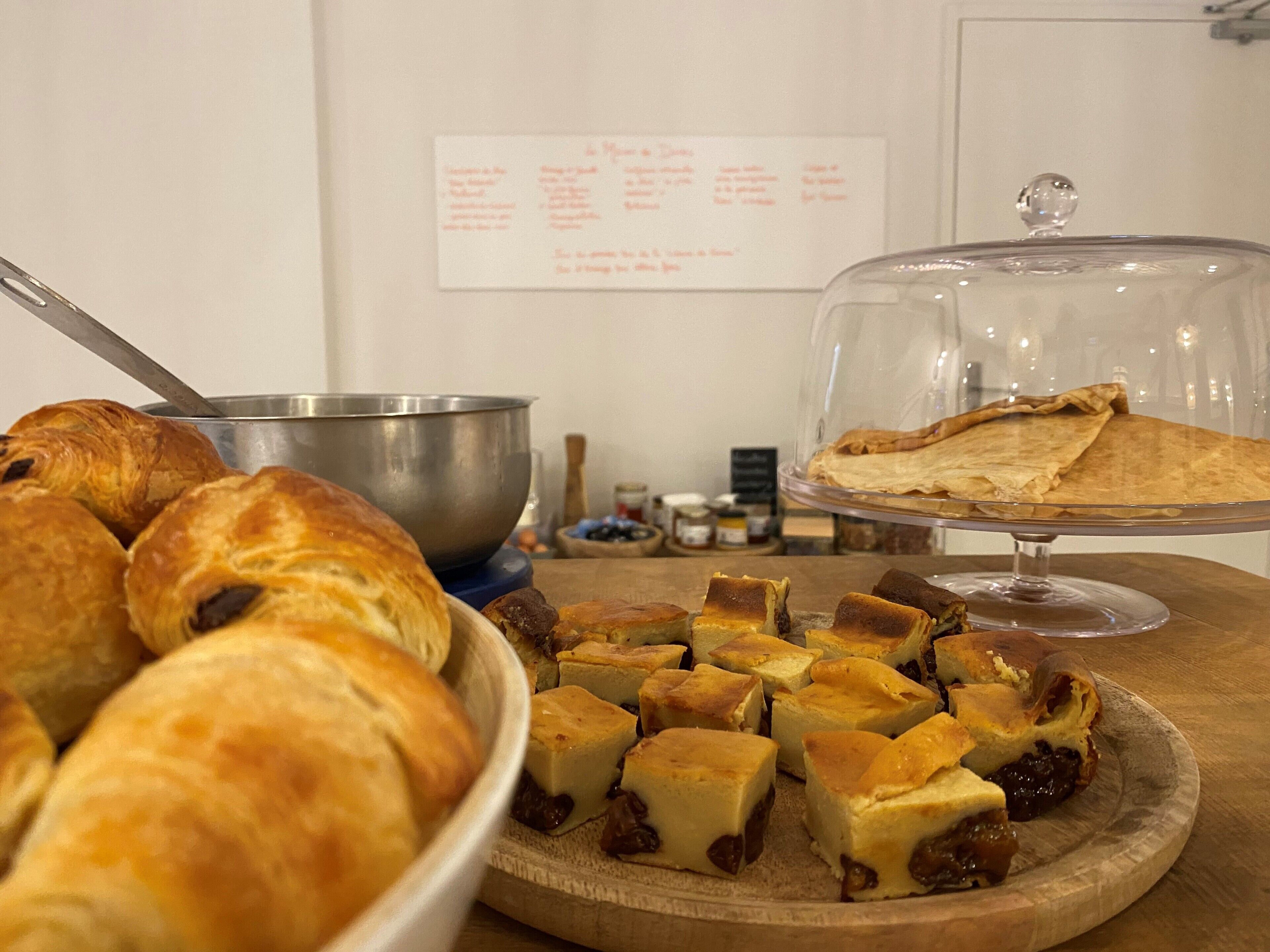 A buffet with various baked goods including croissants, a bowl of soup, and a covered dish of pie.