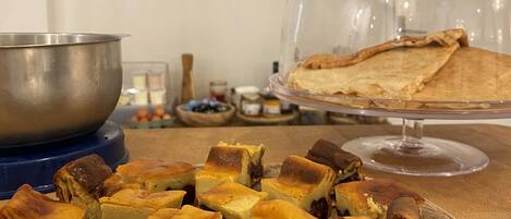 A wooden table with a plate of cheese cubes and a glass display case with a pie.