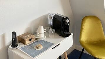 A small, white desk with a black coffee maker, a white cup, a glass container, and a wooden box. A yellow chair is positioned to the right.