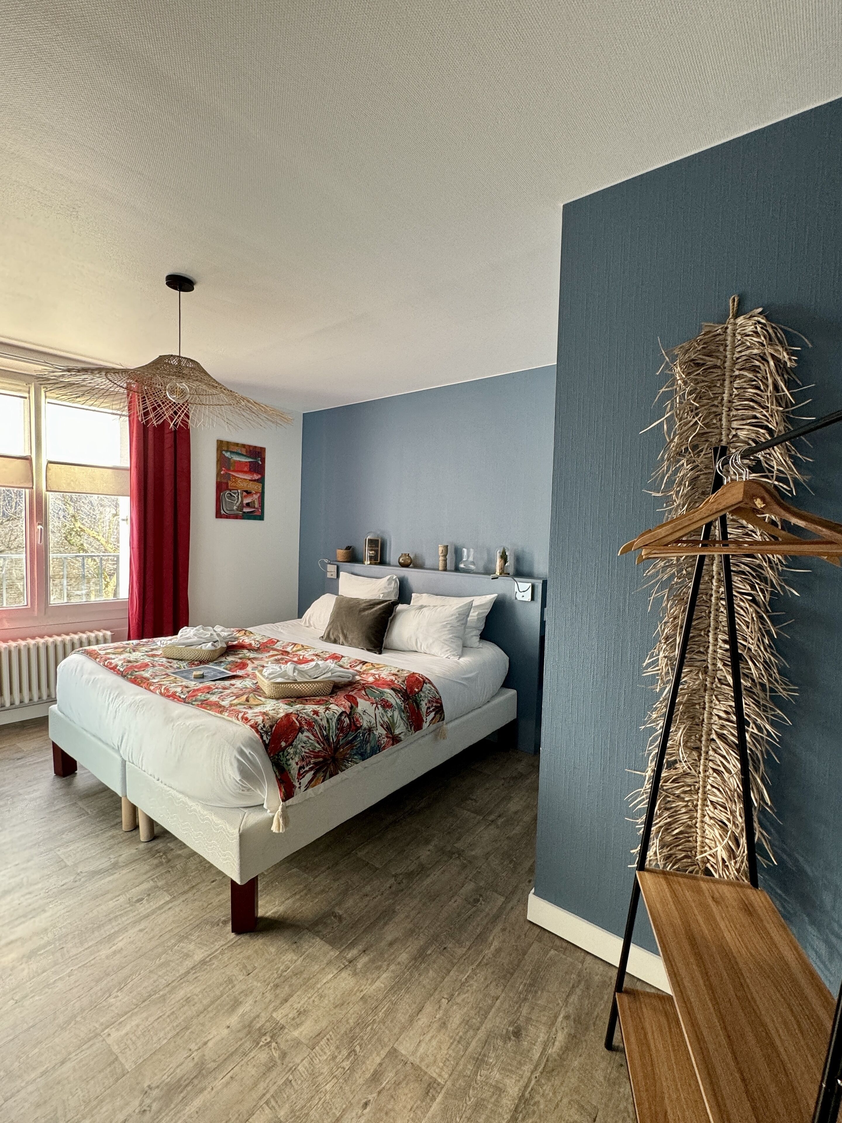 A bedroom with a bed, a hanging light fixture, a wall-mounted coat rack, and a window with curtains.