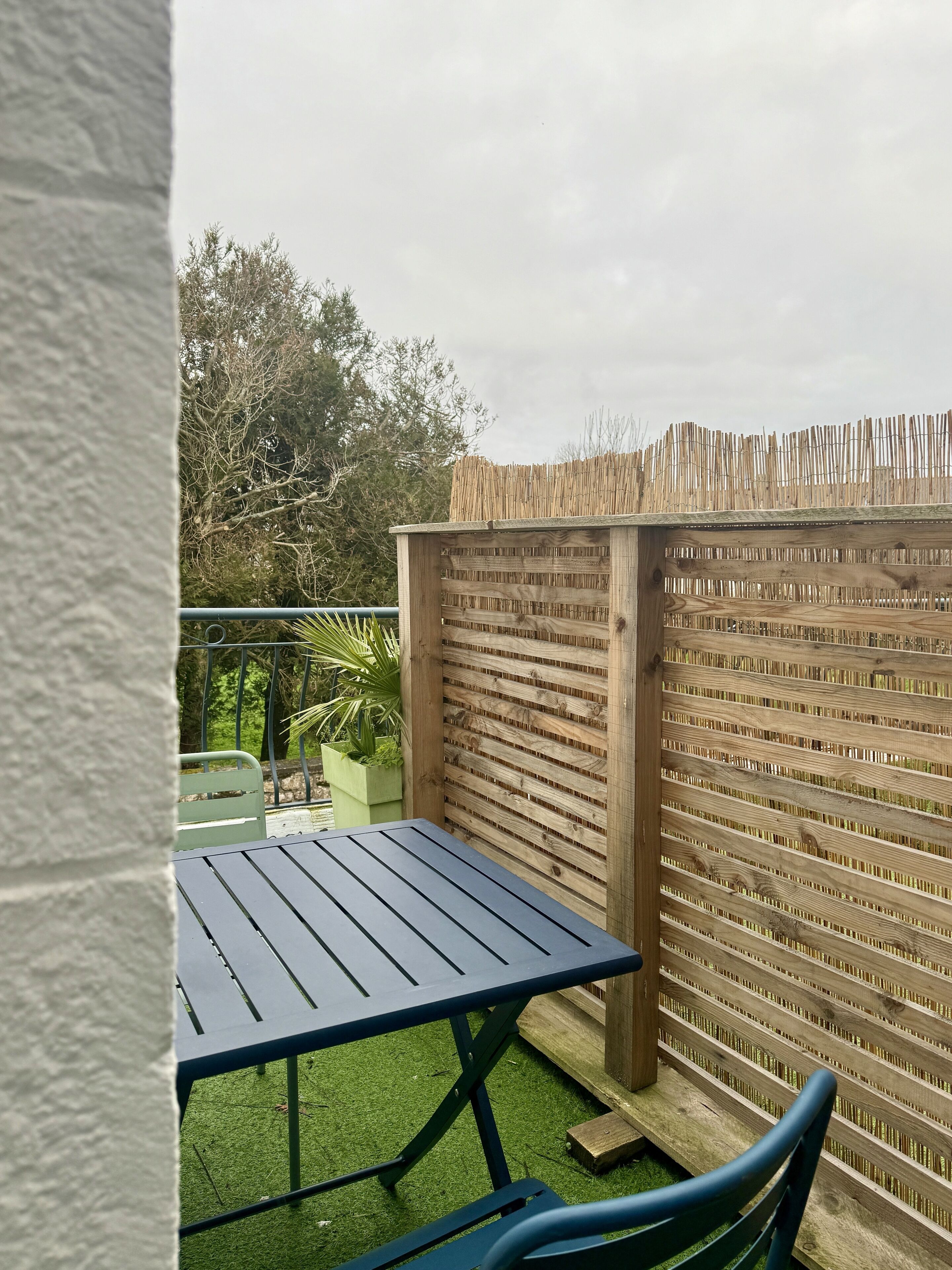 Un patio con una mesa y sillas, cercado por un vallado de madera y con un césped verde.