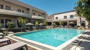 A swimming pool with lounge chairs and umbrellas, surrounded by a multi-story building with balconies.