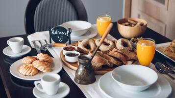 A breakfast setting with plates of pastries, a coffee cup, a glass of orange juice, and a sign reading "Kalimera."