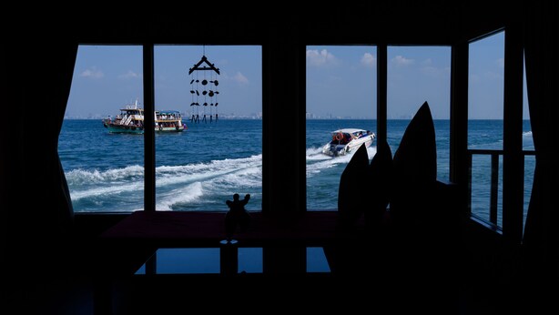 A room with large windows overlooking a body of water, a wind chime, and a small table. - Lareena Resort Koh Larn Pattaya (Koh Lan)