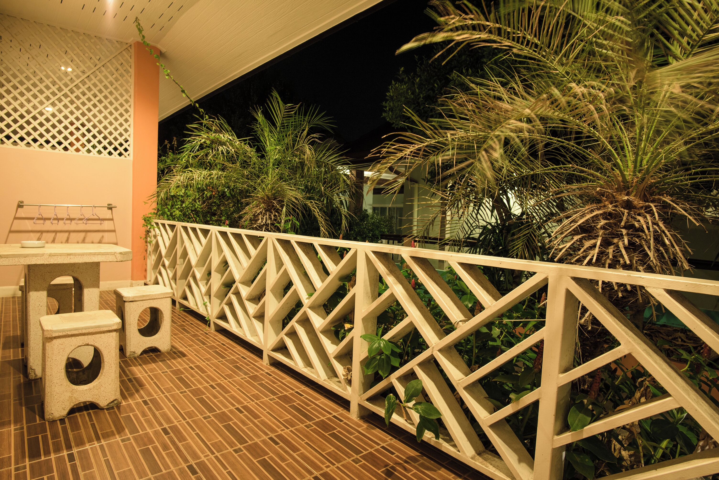 An outdoor patio area with a wooden floor, a white lattice fence, and several potted plants.