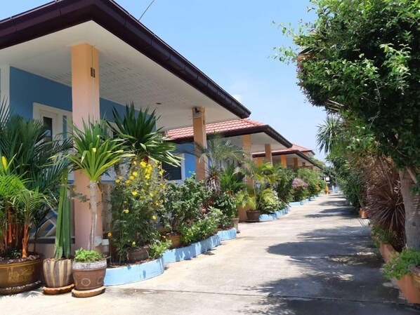 A row of hotel rooms with a covered walkway, surrounded by various potted plants and greenery.