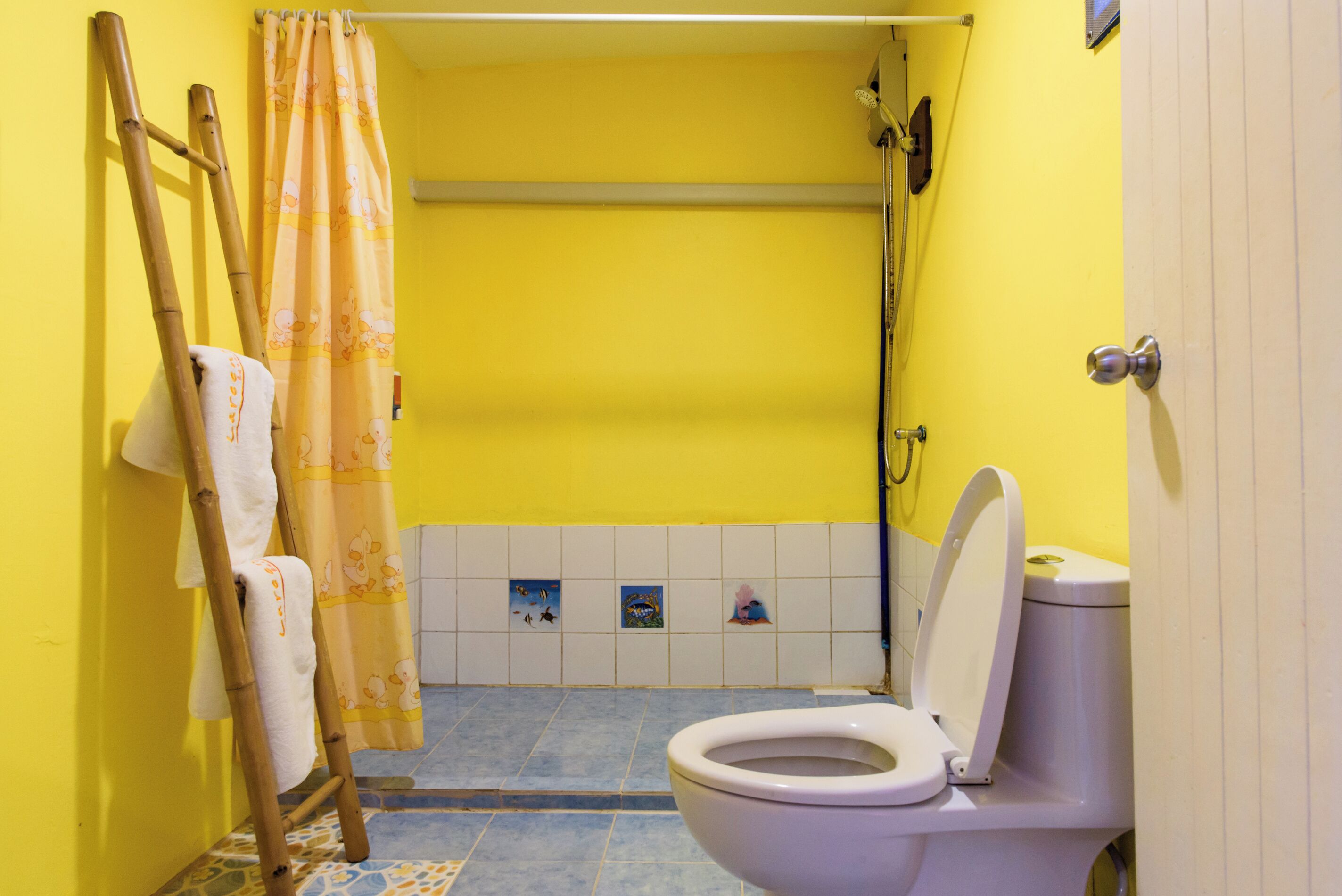 A bathroom with a yellow wall, a white toilet, a shower curtain, and a towel rack.