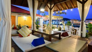 A covered outdoor seating area with wooden tables and benches, surrounded by white curtains and potted plants. - Lareena Resort Koh Larn Pattaya (Koh Lan)