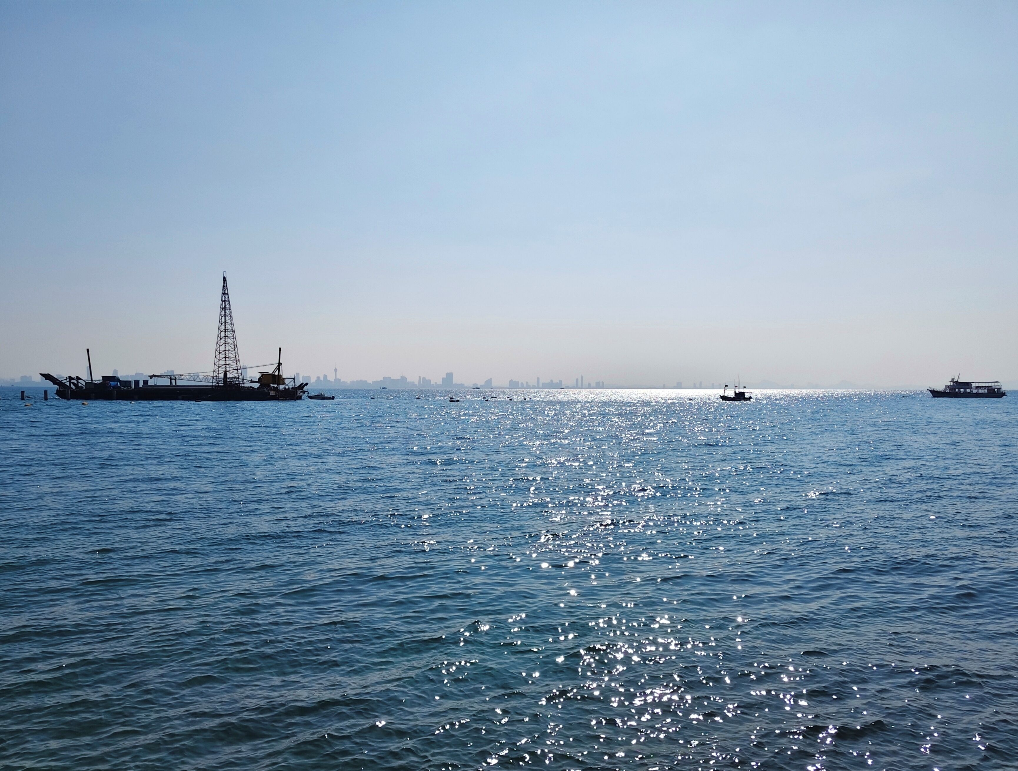 A calm sea with a large ship and smaller boats.