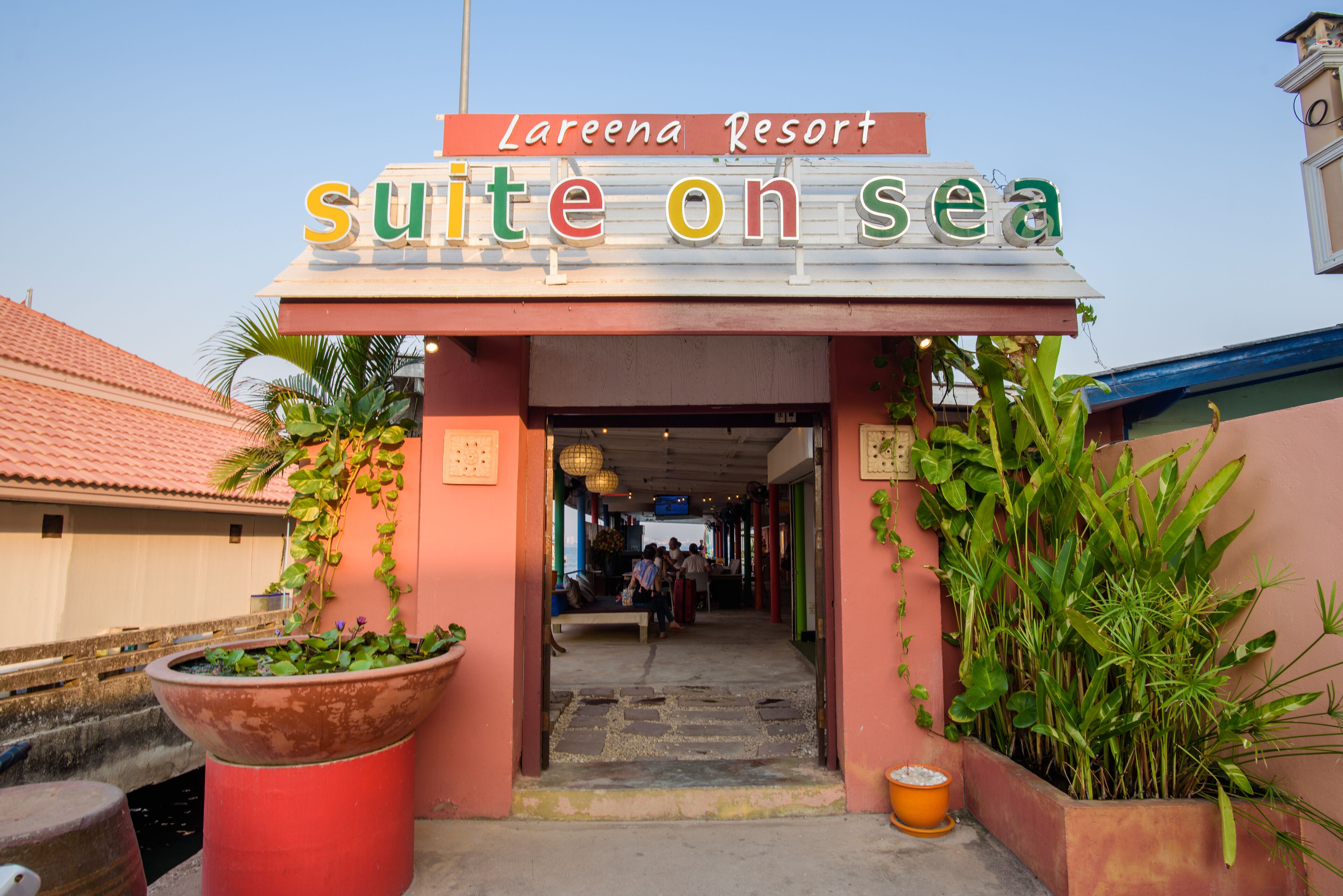 The entrance to Lareena Resort's Suite on Sea, featuring a welcoming archway with a sign, a pathway leading inside, and potted plants on either side.