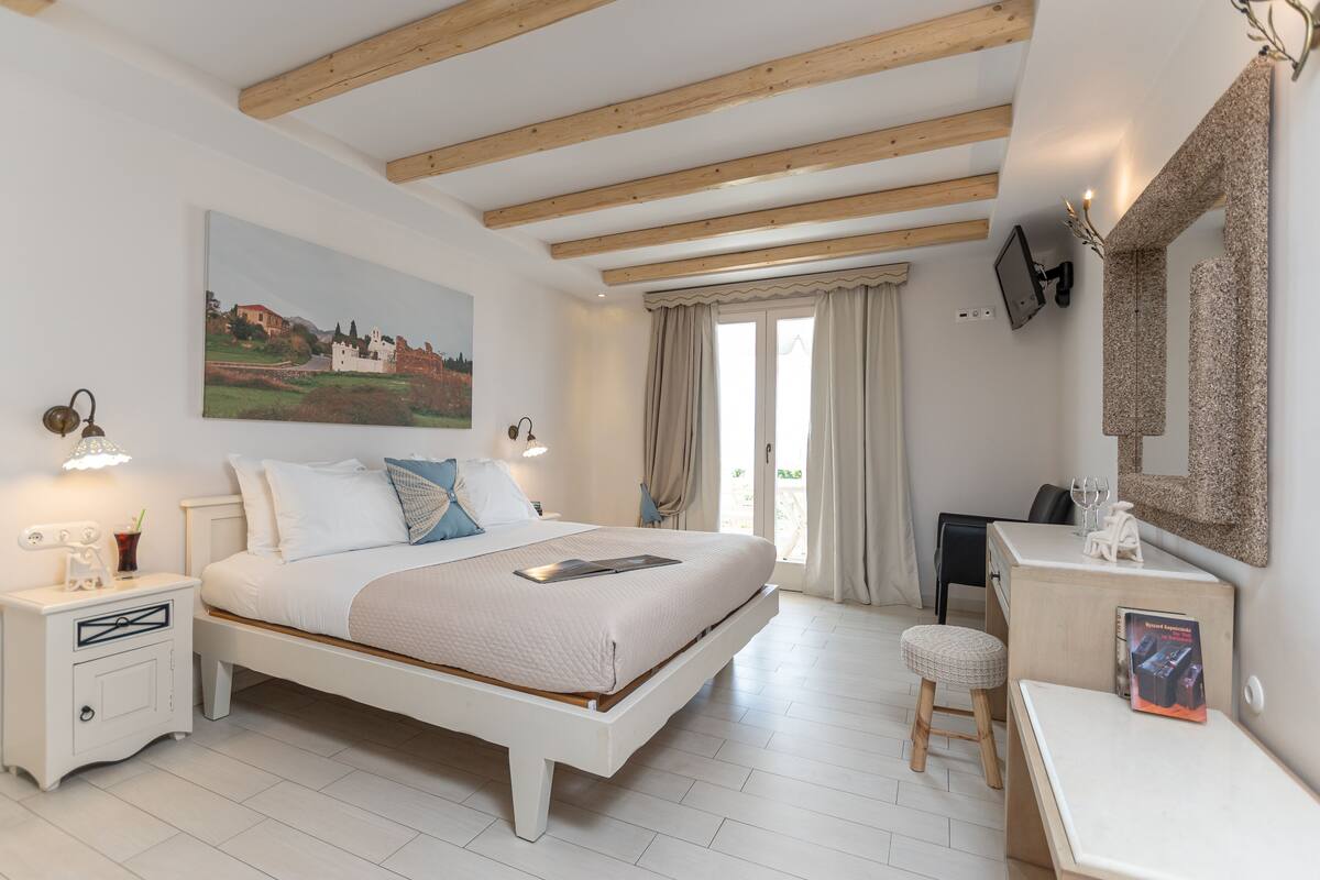 A bedroom with a bed, bedside tables, a desk, a chair, a TV, and a painting on the wall.