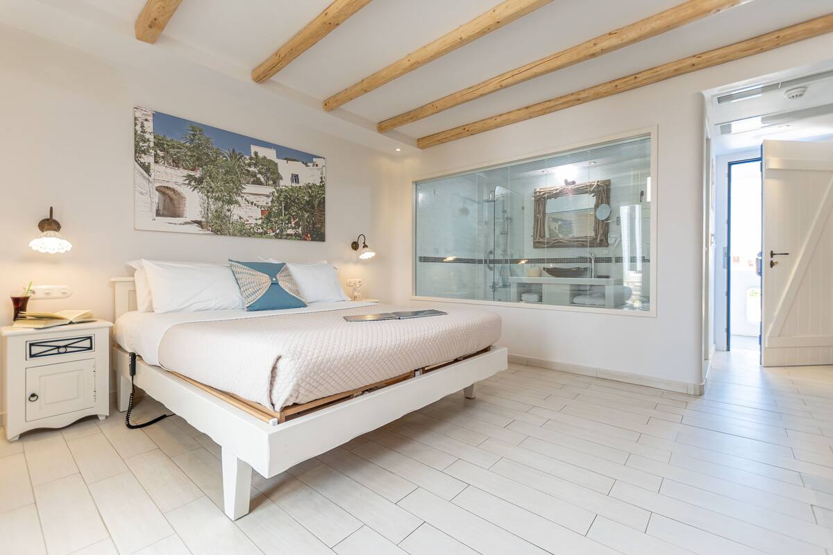 A bedroom with a bed, bedside table, lamp, and a large window with a view of a building.