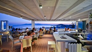 An outdoor dining area with tables and chairs, overlooking a scenic view of the sea and mountains. - Naxos Island Hotel (Naxos)