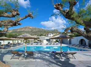 A poolside area with lounge chairs and umbrellas, a clear blue sky, and a mountainous backdrop. - Coriva Beach Hotel (Ierapetra)
