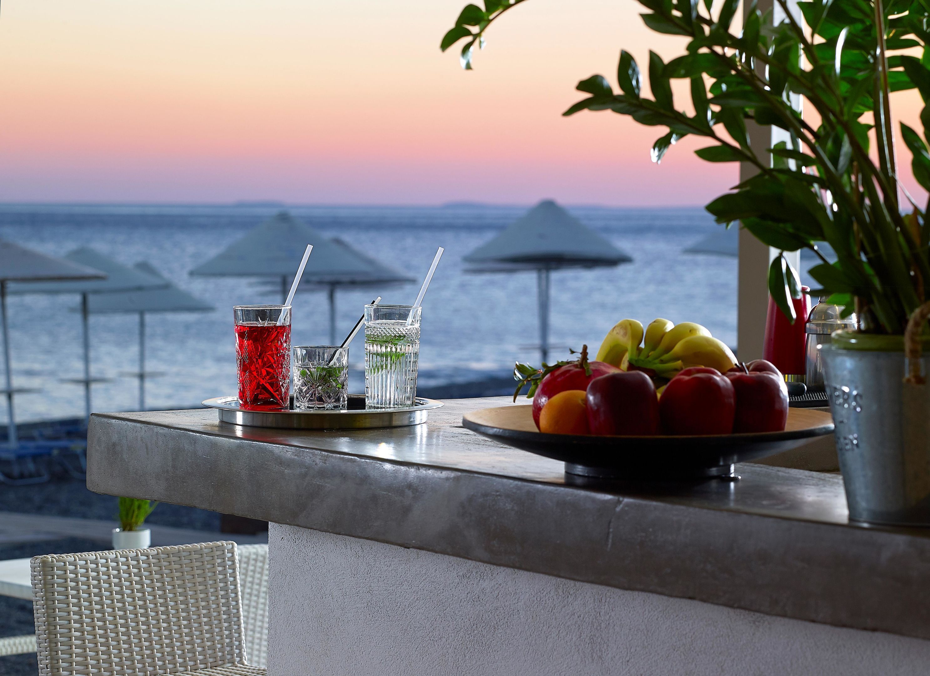 A bar area with drinks and fruits, overlooking a body of water with umbrellas.