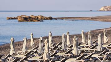 Una playa con filas de tumbonas y sombrillas, afloramientos rocosos en el agua y un cielo despejado.