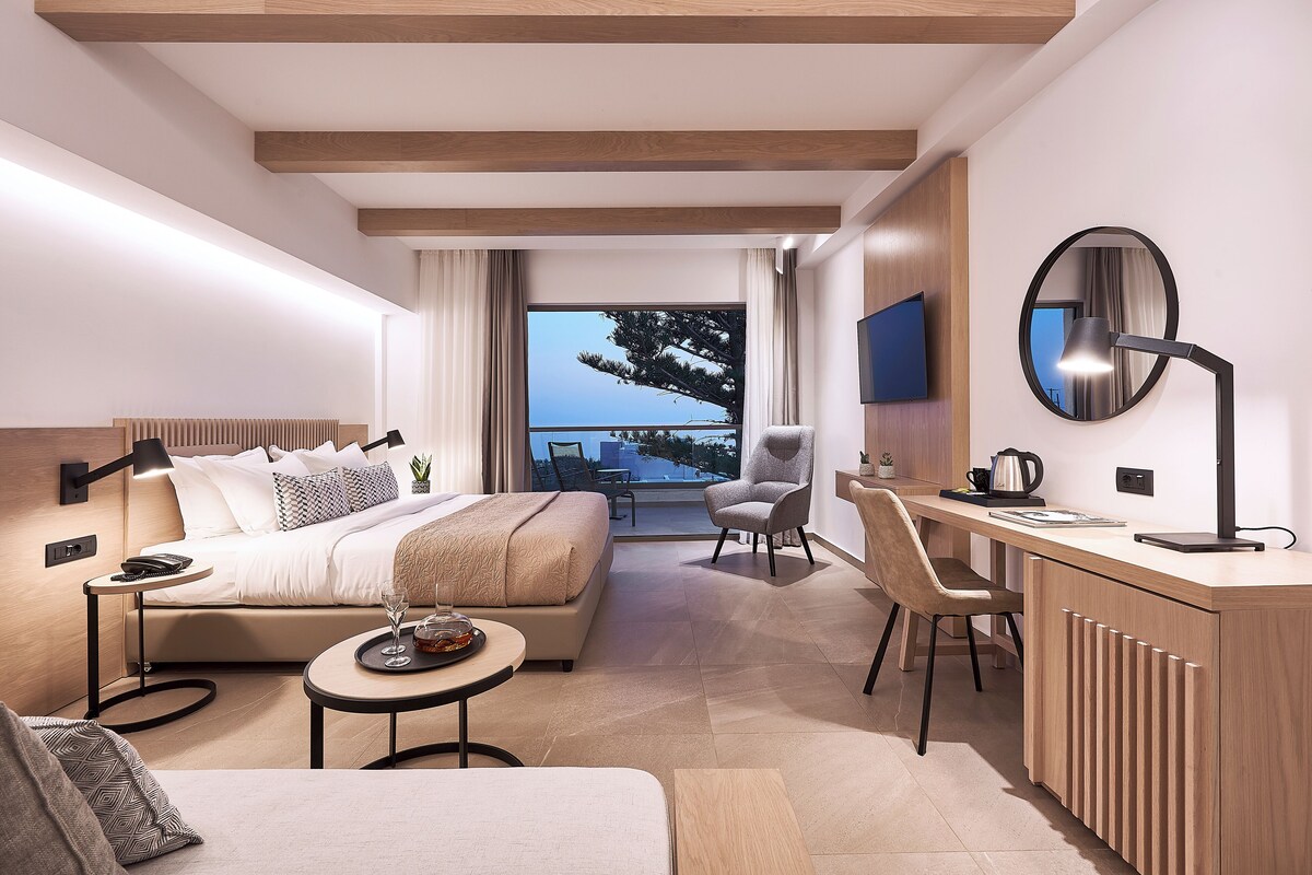 A modern hotel room with a bed, desk, chair, and a view of the outdoors.