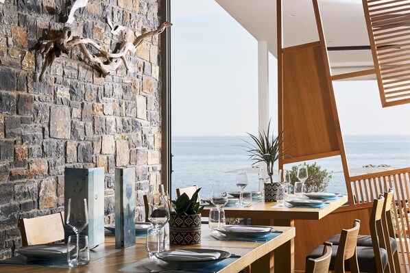 A dining area with a stone wall and a view of the sea. - Coriva Beach Hotel (Ierapetra)