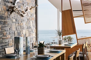 A dining area with a stone wall and a view of the sea. - Coriva Beach Hotel (Ierapetra)