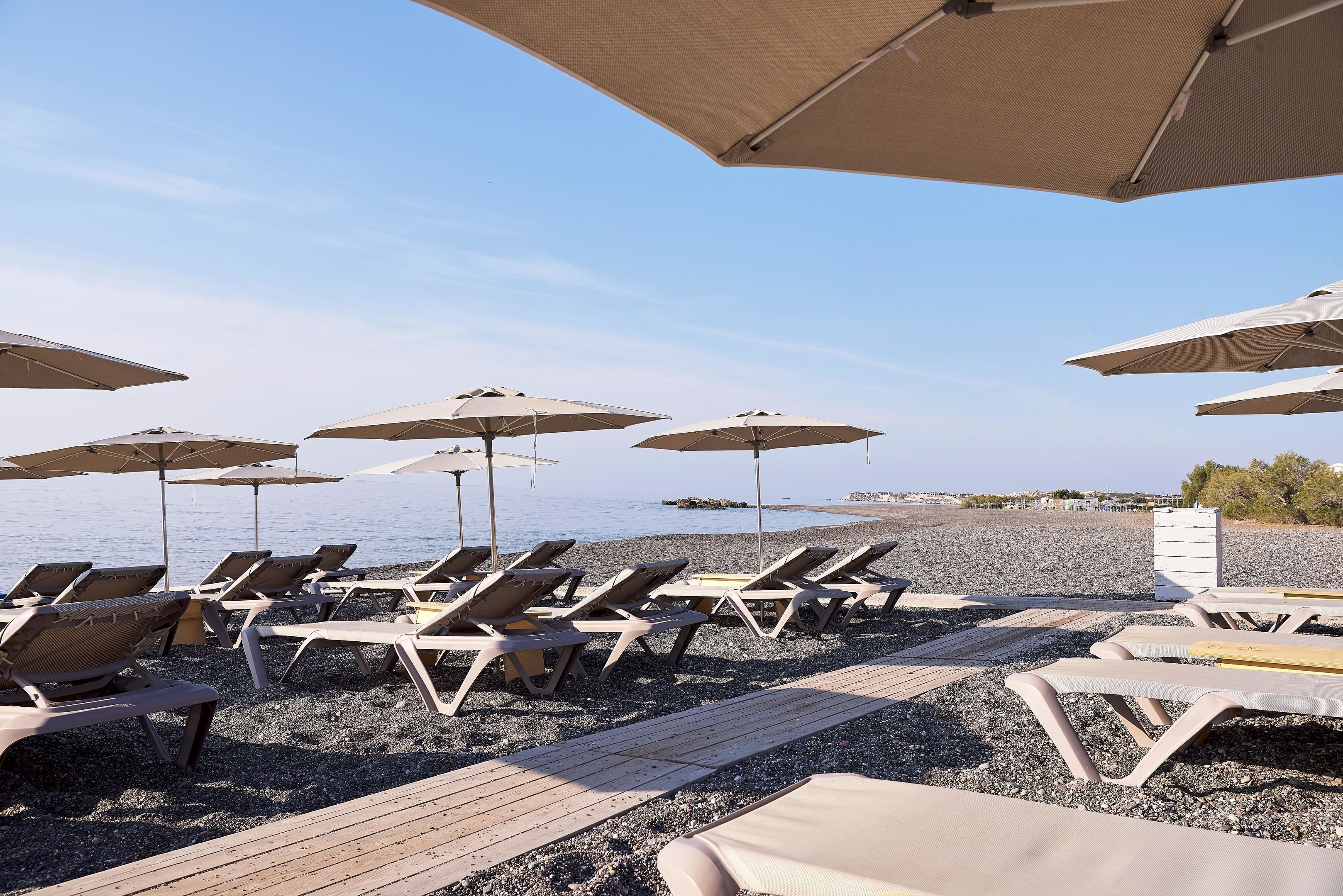 A beachside area with sun loungers and umbrellas, a wooden deck, and a pebble beach.