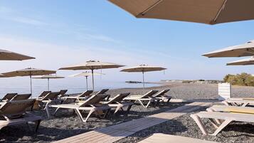 A beachside area with sun loungers and umbrellas, a wooden deck, and a pebble beach.
