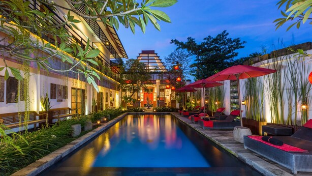 Zona de piscina tranquila con un edificio tradicional al fondo, rodeada de exuberante vegetación y mobiliario de exterior.