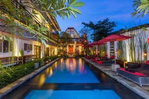 A serene pool area with a traditional building in the background, surrounded by lush greenery and outdoor seating. - Kamar Kamar Rumah Tamu - Boutique Hotel (Denpasar)