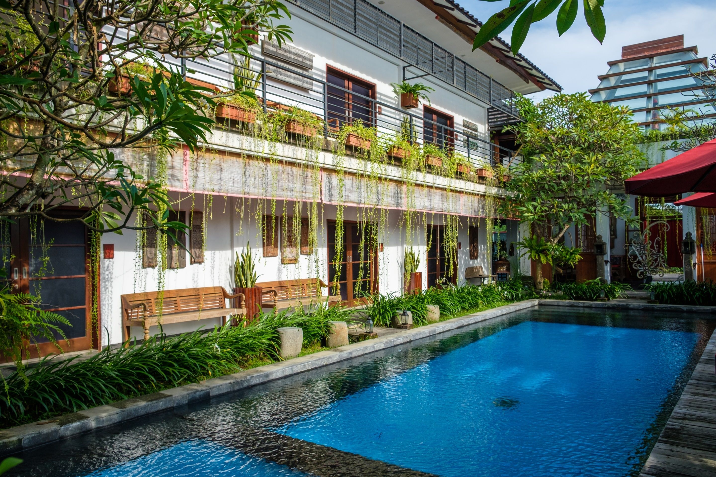 A poolside area with a wooden bench, a white building with balconies, and a clear blue pool.
