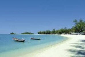 A beach with clear turquoise water, a sandy shore, and two boats anchored near the water's edge. - The Lounge - Hostel (Koh Samui)