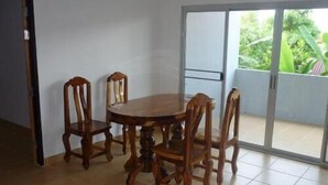 A dining area with a round wooden table and four chairs, a sliding glass door leading to a balcony with greenery. - The Lounge - Hostel (Koh Samui)