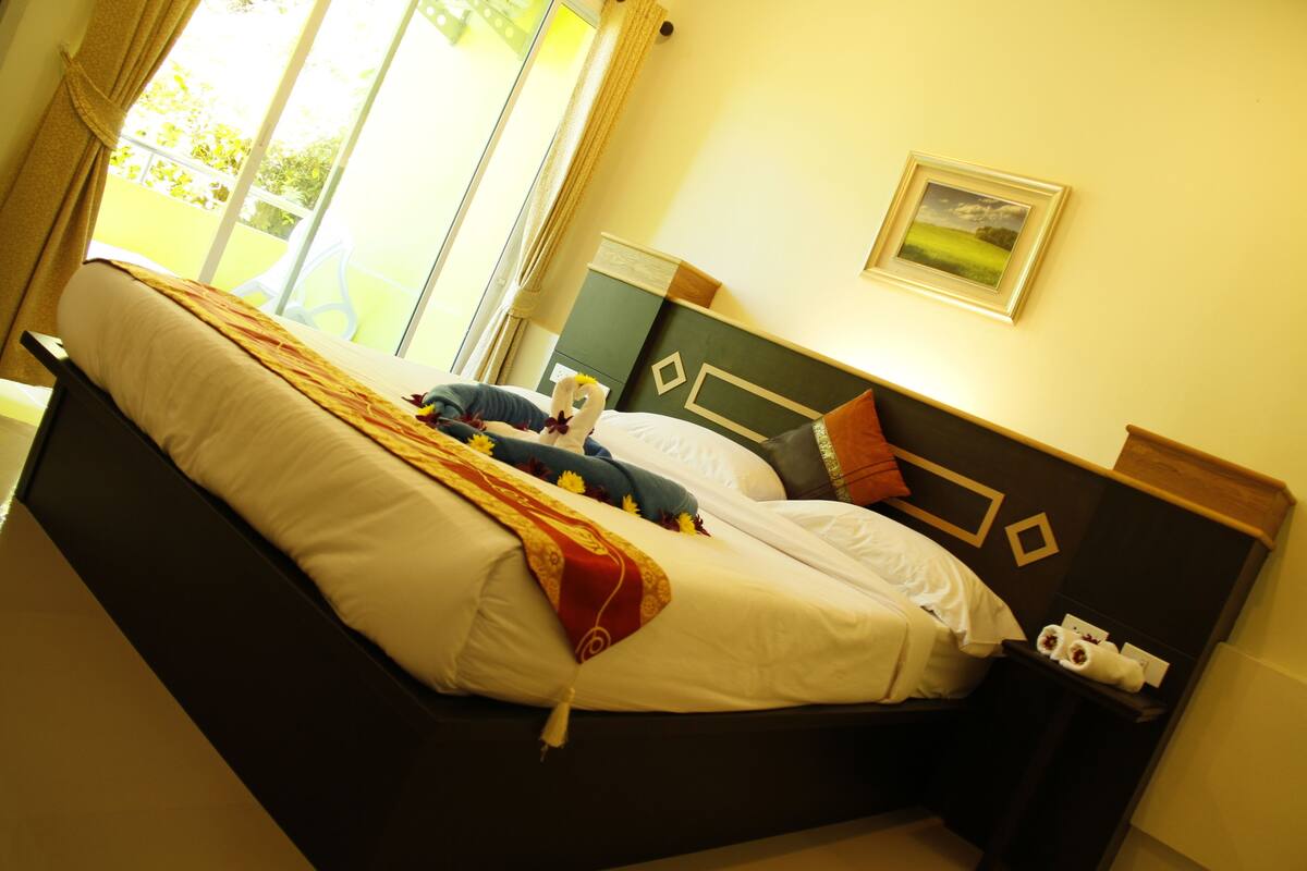 A neatly made bed with a red and yellow blanket, a pillow, and a small decorative item. There is a nightstand with a white lamp and a framed picture on the wall.