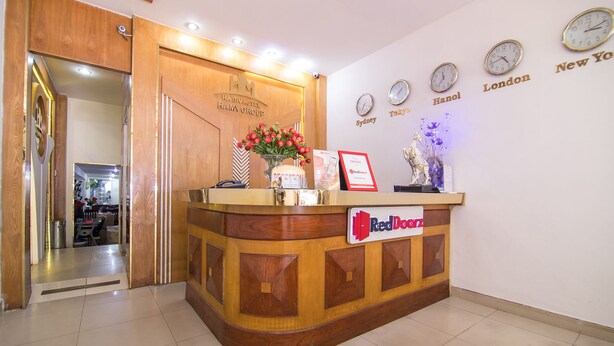 Bancada de recepção de hotel com acabamento em madeira, placa da Red Door e relógios mostrando horários de várias cidades.