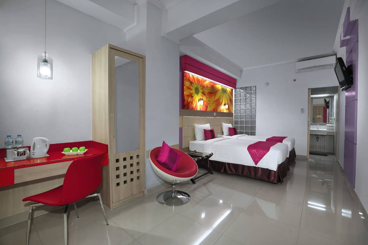A hotel room with a bed, a desk with a chair, a mirror, and a bathroom visible through an open door.