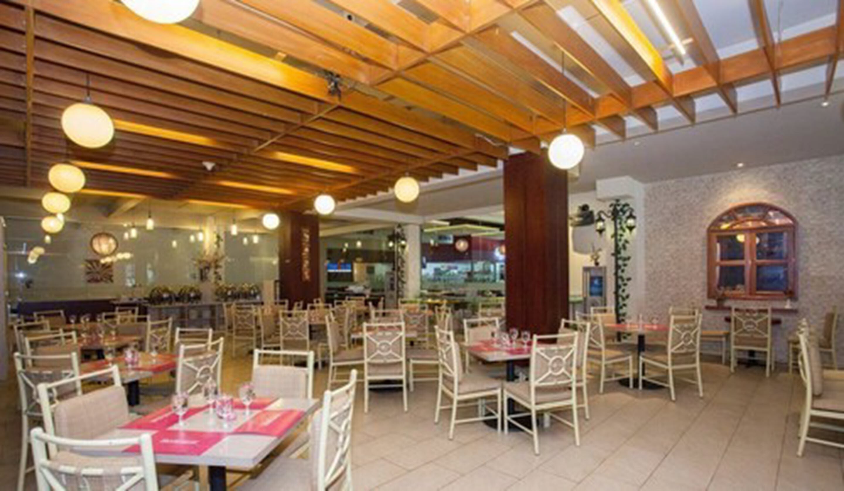 Un restaurante espacioso con vigas de madera en el techo, sillas blancas y mesas dispuestas para comer.